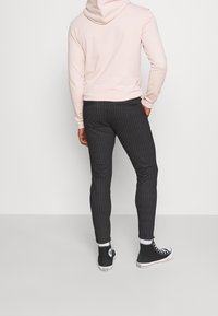 Black pinstripe pants with a slim fit, paired with a light pink hoodie and black high-top sneakers, showcasing a casual look.