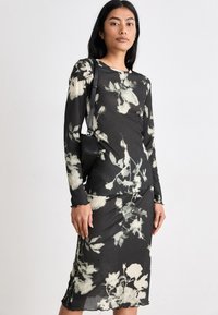 Svart långärmad topp och matchande kjol i blommönster; lättviktsmaterial med ribbad textur; figursydd design; subtila vågiga kanter.