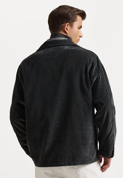 Black corduroy jacket with a collar, featuring vertical ribbed texture and buttoned cuffs, showing a slightly loose fit from the back view.