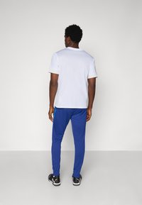 Tricou alb cu mânecă scurtă și decolteu rotund, purtat cu pantaloni albastri conici cu un accent lateral. Pantofi sport negri.