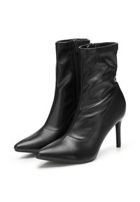 Pár elegantních černých kožených kotníkových bot s špičatou špičkou, bočními zipy a úzkými vysokými podpatky na bílém pozadí.