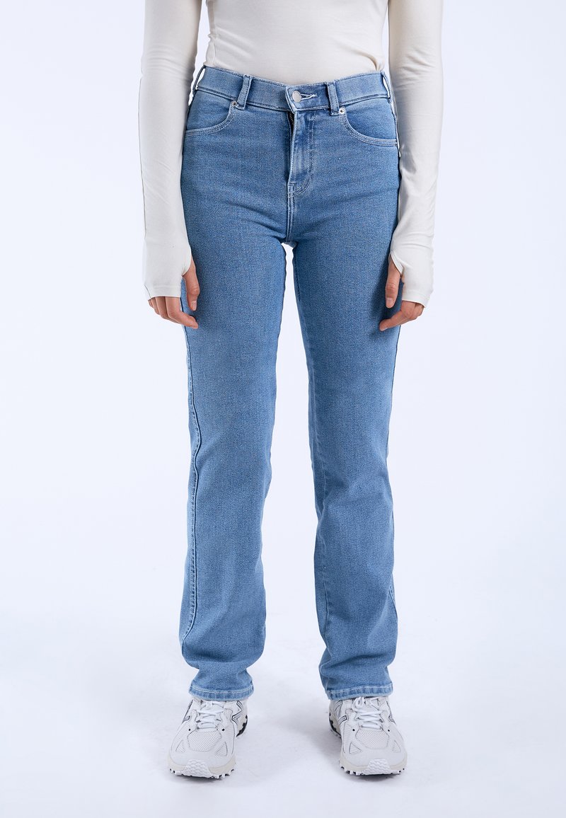 Blue denim jeans with a high waist, straight leg cut, and classic five-pocket design. Worn with a cream long-sleeve top and white sneakers.