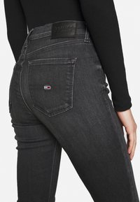 Jeans de denim negro con un diseño ajustado, que cuentan con una etiqueta de cuero en la cintura y un pequeño logo de la marca en el bolsillo trasero.