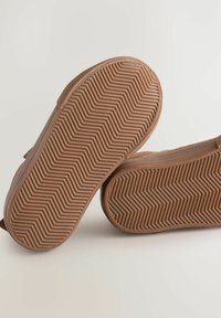 Des chaussures marron à enfiler avec une semelle texturée à motif chevron et un dessus lisse. Le design présente des bords arrondis et des détails minimalistes.