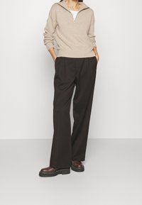 Pull zippé beige en tissu doux, assorti avec un pantalon noir ample et des bottes à plateforme bordeaux. Coupe décontractée, sans motifs ni accents.