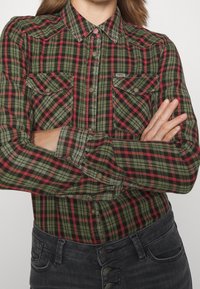 Camicia a quadri multicolore in verde, rosso e nero, con colletto, chiusura a bottoni e due tasche frontali. Tessuto morbido, maniche lunghe.