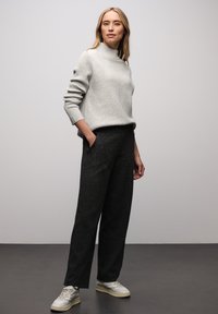 Hellgrauer, gerippter Pullover mit Stehkragen, kombiniert mit dunklen, strukturierten Hosen mit weitem Bein und hellen Sneakers, vor einem schlichten Hintergrund.