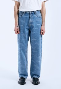 Vaqueros de mezclilla azul claro con un corte relajado, que presentan patrones de texto impresos, diseño de cinco bolsillos y una silueta de pierna recta.