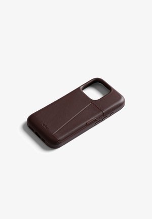 Étui de téléphone en cuir brun foncé avec un support pliable intégré, découpes pour l'appareil photo et les boutons, incliné sur un fond blanc.