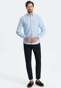 Lichtblauw overhemd met lange mouwen, gecombineerd met donkere slim-fit broeken en donkere schoenen. Eenvoudig ontwerp, geen patronen of accenten.