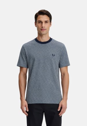 Hombre vistiendo una camiseta de manga corta con cuello redondo y cuadros en azul marino y blanco, y pantalones negros, de pie frente a un fondo liso.