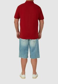 Rotes Baumwoll-Polohemd mit kurzen Ärmeln, kombiniert mit hellblauen Denim-Shorts. Das Outfit wird mit weißen Sneakers abgerundet.