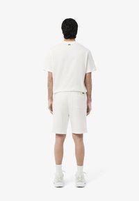 Conjunto de camiseta blanca de algodón de manga corta y pantalones cortos. La camiseta tiene un logo verde en la parte trasera, cuenta con un corte relajado y los pantalones cortos tienen un bolsillo en la parte trasera.
