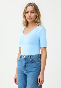 Lichtblauwe, kortapondd bodysuit met een V-hals ontwerp, gemaakt van glad materiaal, gecombineerd met hoge taille blauwe denim jeans.