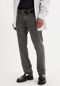 Grå denim jeans med rett snitt, med en subtil slitt tekstur og klassisk femlommers stil, sammen med et svart belte og sko.