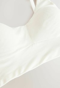 Witte beha van gladde stof, met een gebogen vorm en dunne verstelbare bandjes. Het ontwerp bevat subtiele naaddetails en geen patronen.
