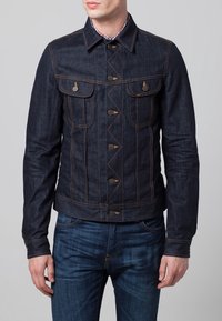 Mörkblå denimjacka med en strukturerad design, utrustad med två bröstfickor, gyllene beslag och kontrasterande orange sömmar.