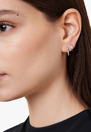 Silver hoop earrings with a textured pattern, featuring three stacked designs: one embellished with clear stones, one smooth, and one straight bar.