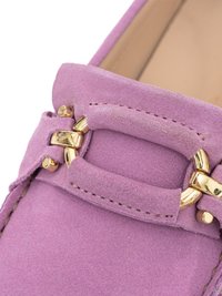 Close-up of a purple suede loafer with gold metal horsebit detail on the upper front part of the shoe.
