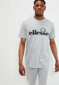 Camiseta gris de manga corta con un logo negro de "ellesse". Fabricada con una tela suave, con un corte holgado y un clásico cuello redondo.