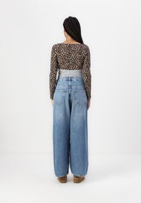 Leopard print long-sleeve top, gray waistband, paired with wide-leg blue denim jeans. Casual, loose fit, with a textured fabric.