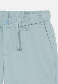 Pantalones azul claro con cintura elástica, cordón ajustable y cierre de un solo botón, con una textura sutil.