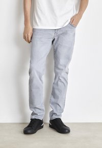 Jeans grigi chiari con una vestibilità a gamba dritta, realizzati in denim. Abbinati a sneaker nere con dettagli bianchi. Design semplice e casual.
