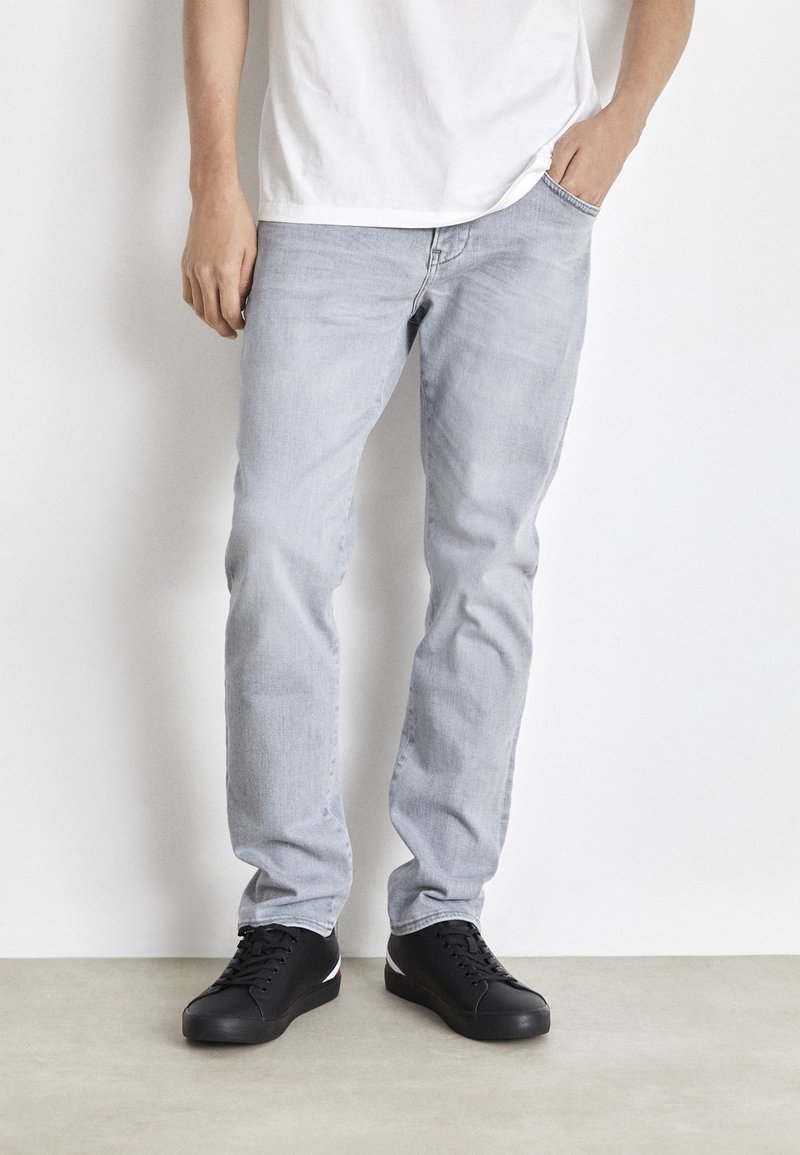 Jeans grigi chiari con una vestibilità a gamba dritta, realizzati in denim. Abbinati a sneaker nere con dettagli bianchi. Design semplice e casual.