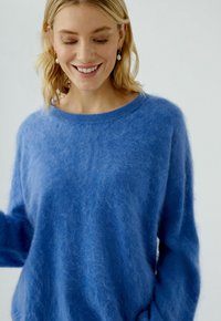 Blauw harig sweatshirt gemaakt van zacht materiaal, met een ronde halslijn en lange mouwen. De structuur lijkt pluizig, met een losse pasvorm.