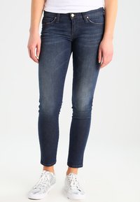 Smal passform, mörkblå denimjeans med en blekt tvätt, med fem fickor och kopparfärgad hårdvara, i kombination med silvriga sneakers.