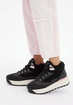 Black footwear with a textured, fluffy upper, featuring gray accents, metal hooks, and a thick white sole with a pink trim.