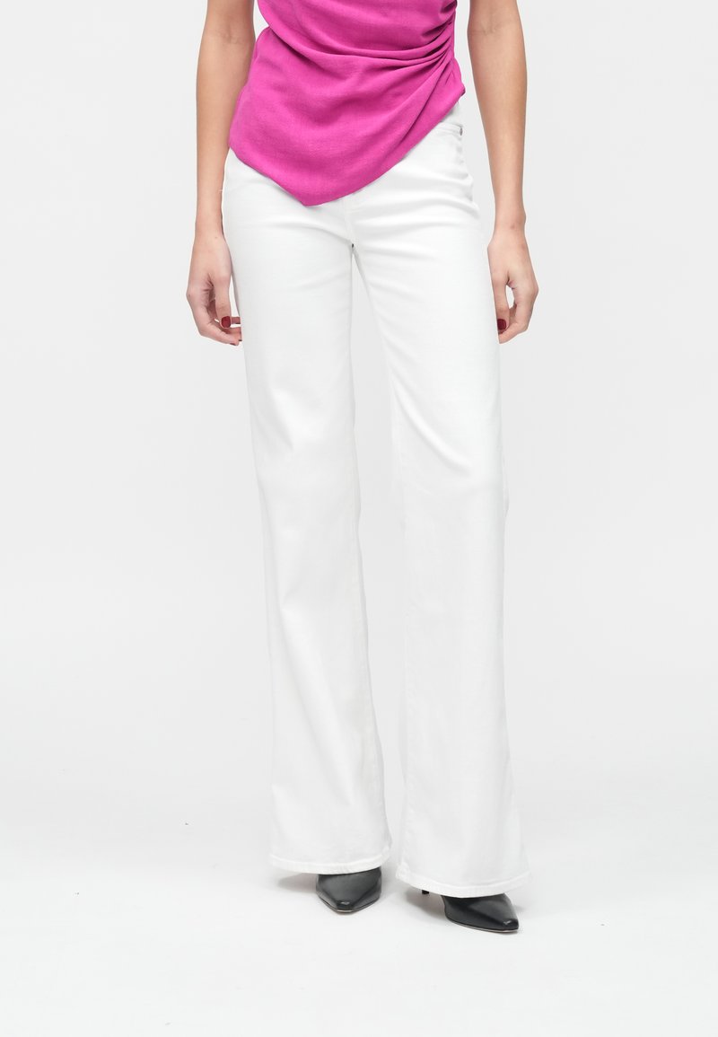 Witte uitlopende broek met een gladde textuur, voorzien van een hoge taille en steekzakken aan de voorkant, gecombineerd met een roze top en zwarte hakken.