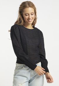 Sort bluse med broderede blomster mønstre, lange puffærmer og rund halsudskæring, parret med lyseblå slidte jeans.