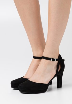 Chaussures à talons hauts en suede noir avec un bout arrondi, une sangle à la cheville et une boucle carrée. Les talons ont une hauteur modérée, complétant le design élégant.
