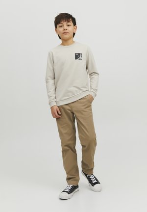 Felpa grigia chiara con una piccola grafica nera sul petto, abbinata a pantaloni beige e sneakers nere con suole bianche.