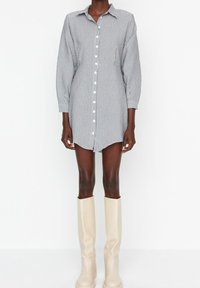 Robe chemise rayée en blanc et marine, design à boutons sur le devant, manches longues, ourlet asymétrique, associée à des bottes crèmes jusqu'aux genoux.