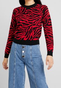 Červeno-černý svetr s pruhy ve vzoru zebry, kulatým výstřihem a žebrovanými manžetami. Spárován s vysokými světle modrými širokými džíny s knoflíky.