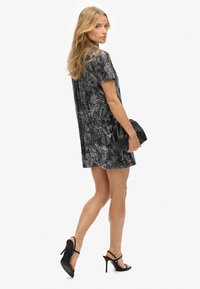 Vestido negro con estampado plateado de manga corta, hasta la rodilla, combinado con un bolso de mano negro y sandalias de tacón alto. Textura suave, corte relajado.