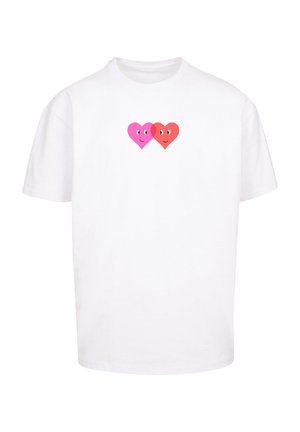 Biela bavlnená tričko s centrálnou grafikou dvoch usmievajúcich sa srdcí, jedným ružovým a druhým červeným, s výraznými očami.