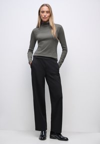 Olivgrön ribbad polotröja, smal passform, kombinerad med svart vidbyxade byxor med hög midja och svarta ankelboots. Enkel, modern design.