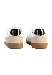 Sneakers bianchi con accenti neri sul tallone, suola in gomma beige e tessuto testurizzato. Presentano una forma arrotondata e un design semplice.