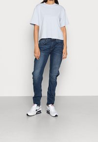 Ljusblåkortärmad t-shirt, mörkblå jeans med lätt blekning, och vita sneakers med marinblå och röda accenter, vilket skapar en avslappnad outfit.