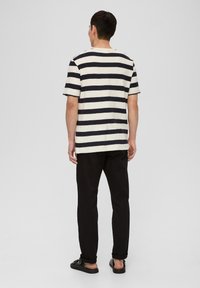 Camiseta a rayas en color crema y marino, de mangas cortas, con un corte holgado, vista desde la espalda. Combinada con pantalones negros y sandalias.