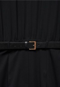 Tissu noir ceinturé à la taille avec une fine ceinture en cuir noir ornée d'une boucle rectangulaire dorée.