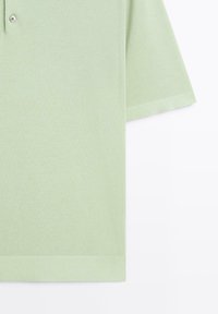 Polo shirt di colore verde chiaro, con maniche corte, colletto abbottonato e orlo e polsini a costine. Texture del tessuto liscia e morbida.