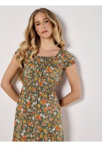 Blumenkleid in Grün mit orangefarbenen, gelben und weißen Blumen. Verfügt über kurze Ärmel, einen quadratischen Ausschnitt und Raffung an der Taille.