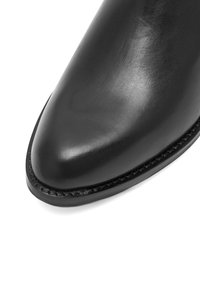 Czarny skórzany but z szpiczastym noskiem i gładką fakturą. Posiada przeszyte czarne detale na podeszwie.