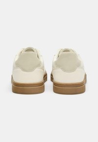 Weiße Ledersneaker mit glatter Oberfläche, abgerundetem Fersenteil und hellbraunen Gummisohlen. Minimalistisches Design mit sanften Texturakzenten.