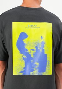 Black t-shirt featuring a large graphic on the back with a yellow background and blue abstract shapes, labeled "REPLAY DEEP FREQUENCIES."