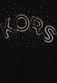 Svart tyg med ordet "KORS" i guldomfattade bokstäver, dekorerade med små silvernitar i ett prickmönster runt texten.